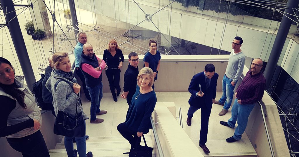 A group of travel professionals standing on a modern staircase during a familiarization trip, smiling and posing in a contemporary building with glass and steel elements.