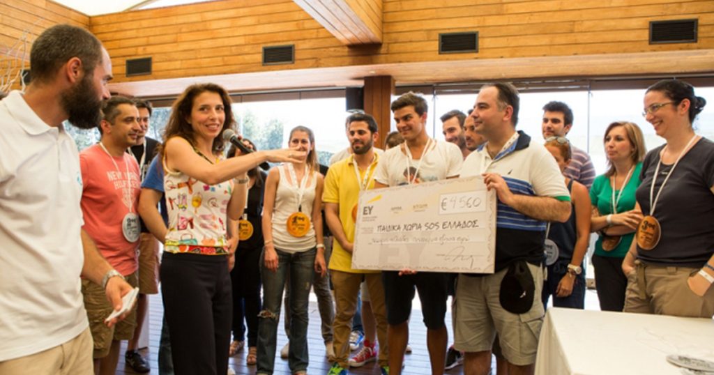 Team members from Ernst & Young’s auditing department gathered indoors, smiling and presenting a large donation cheque to SOS Children’s Villages Greece, during a CSR and team bonding event.
