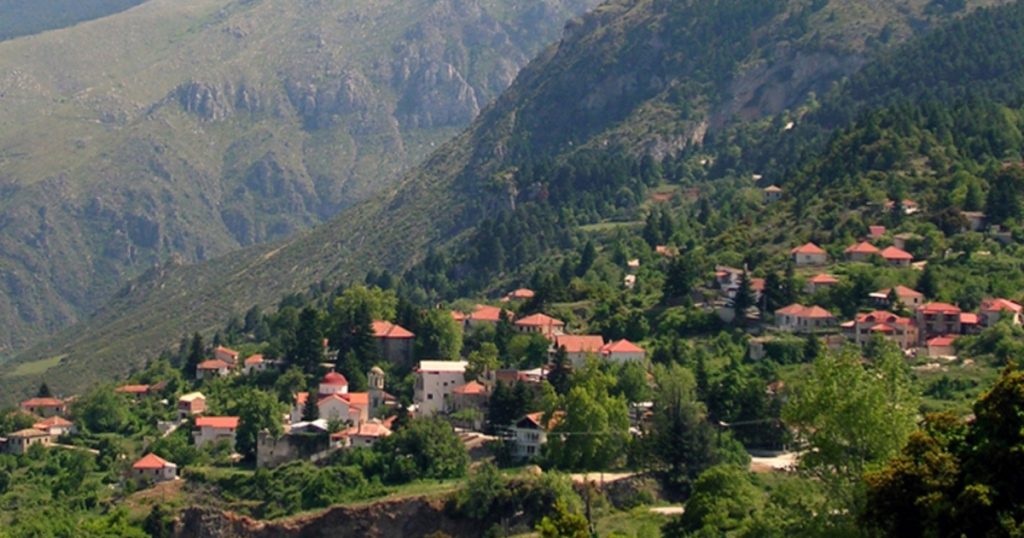 Mountain village with red-roofed houses nestled in lush greenery, surrounded by dramatic slopes, location of the EKOGI Scientific Meeting.