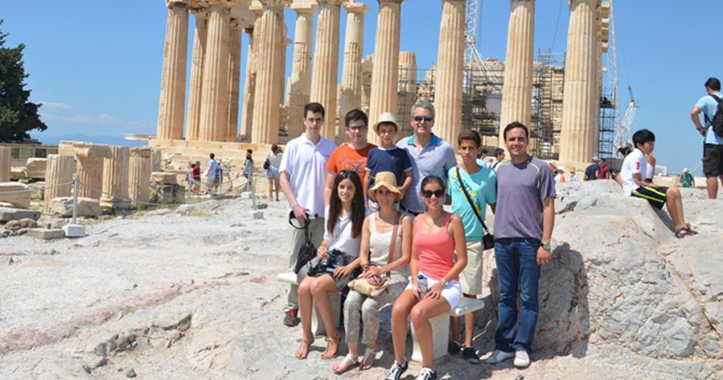 Multigenerational family posing in front of the Parthenon on the Acropolis in Athens, enjoying a sunny day during their cultural holiday in Greece.