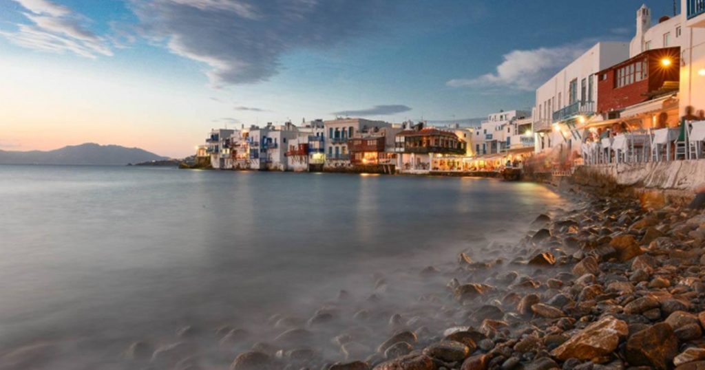 Scenic evening view of Little Venice in Mykonos, Greece, with colorful waterfront houses and restaurants illuminated by warm lights, reflecting the charm of the Greek islands.