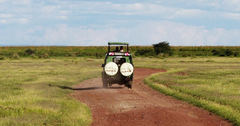 4x4 safari vehicle driving on a dirt road across the Tanzanian savannah under a partly cloudy sky, as part of Interasco's incentive journey.