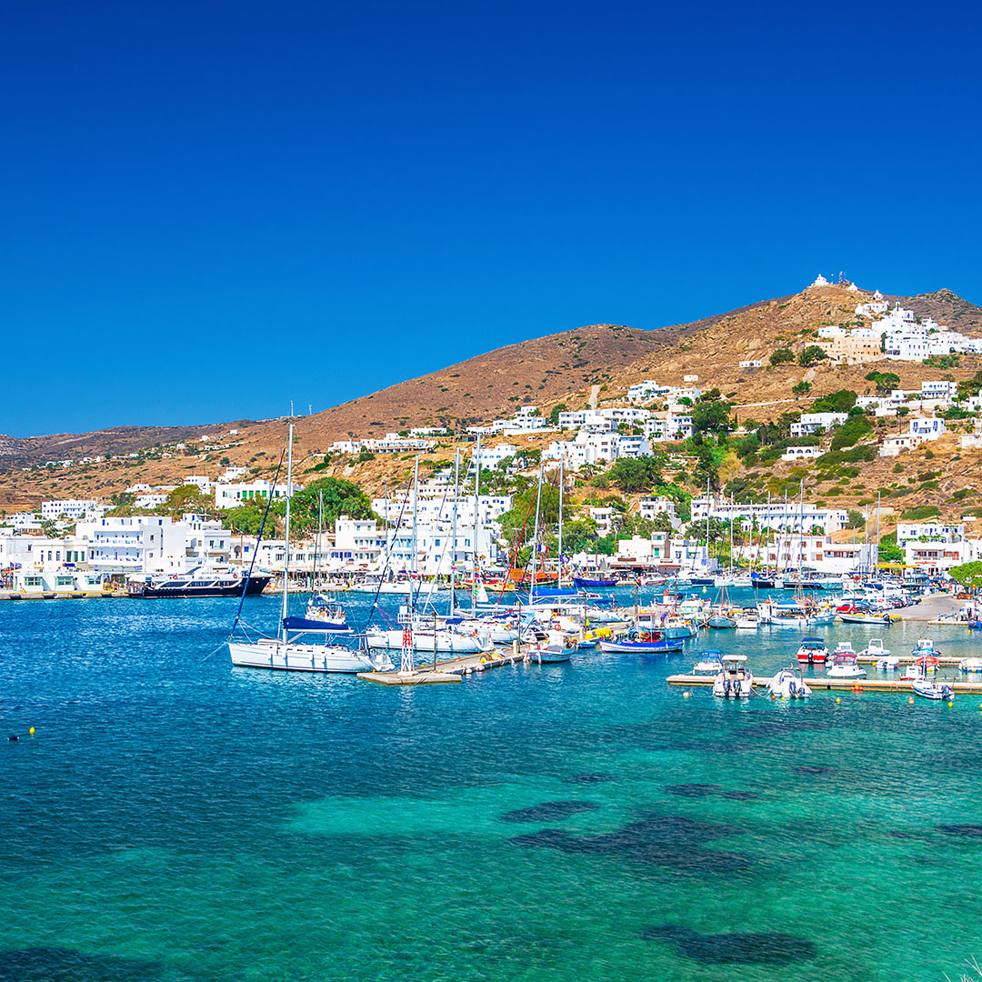 Harbor view of Ios island, Greece, with colorful boats, turquoise waters, and hillside whitewashed houses.