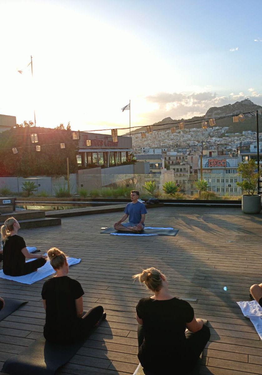 Group practicing rooftop yoga in Athens during a corporate fashion industry meeting organized by feelosophy.
