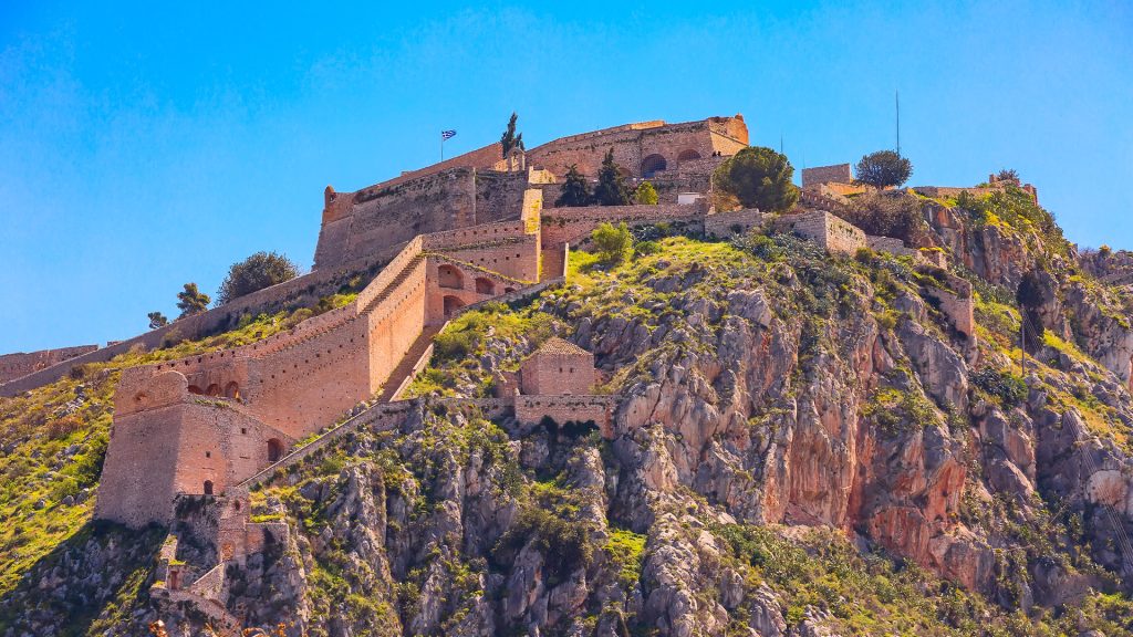 Close-up view of the Palamidi Fortress atop a rocky hill in Nafplio, Greece, under a bright blue sky.