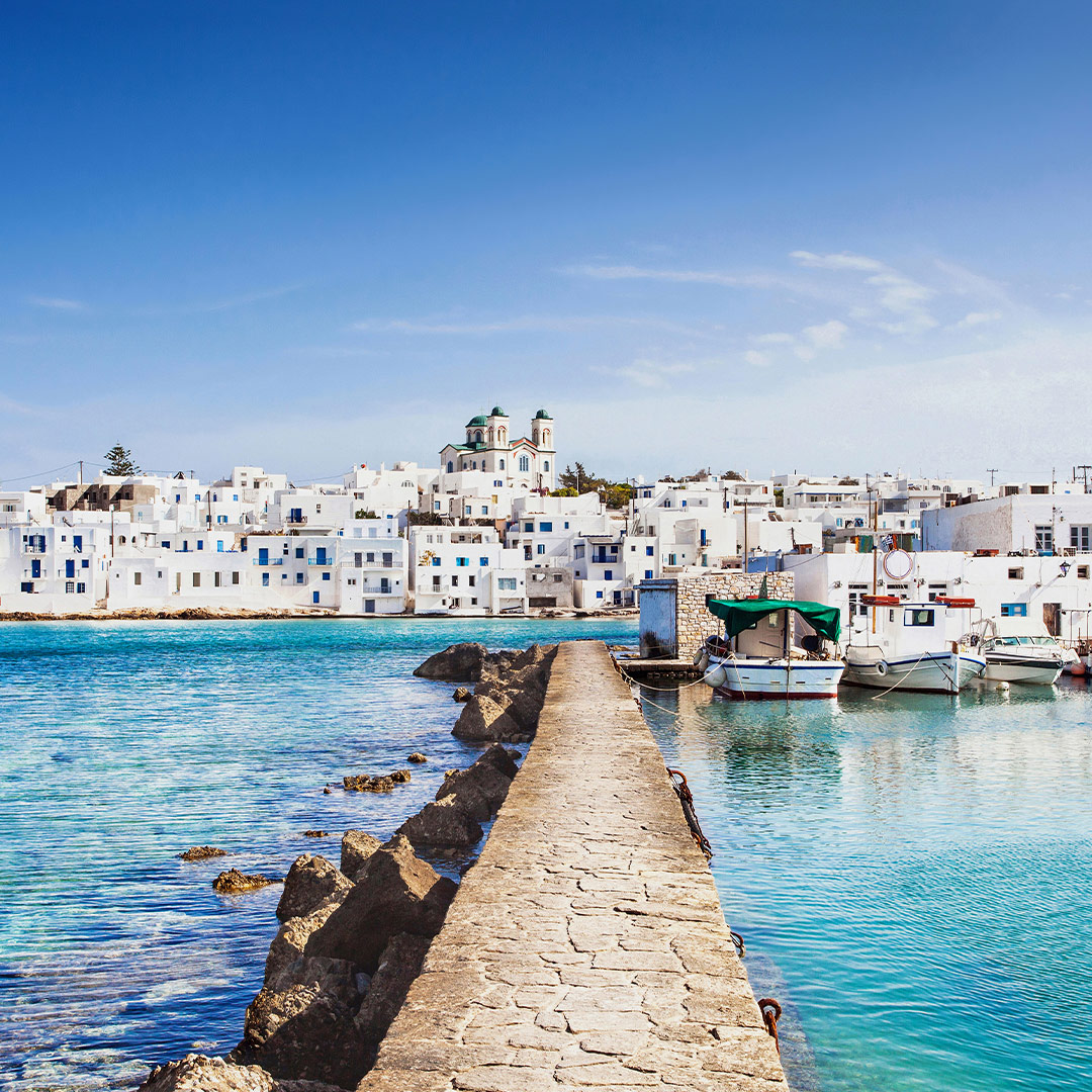 Scenic view of Naoussa in Paros, Greece, with whitewashed houses, fishing boats, and turquoise Aegean waters.