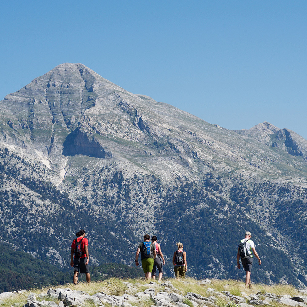 Group of hikers trekking on mountain trails in Greece with dramatic peaks in the background during The Root retreat.