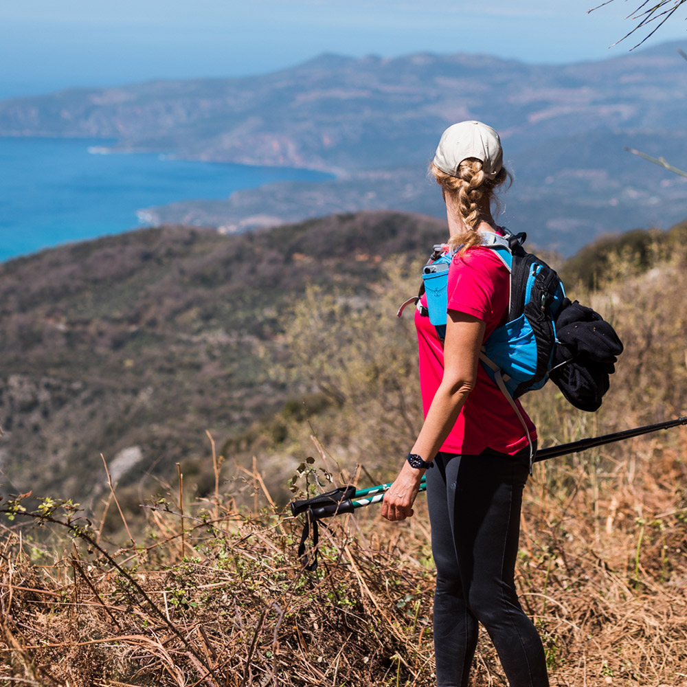 Woman hiking on a mountain trail overlooking the sea during The Root wellness retreat in Greece.
