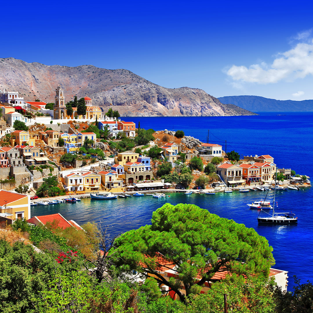 Colorful neoclassical houses by the harbor of Symi island, Greece, with boats on deep blue Aegean waters.