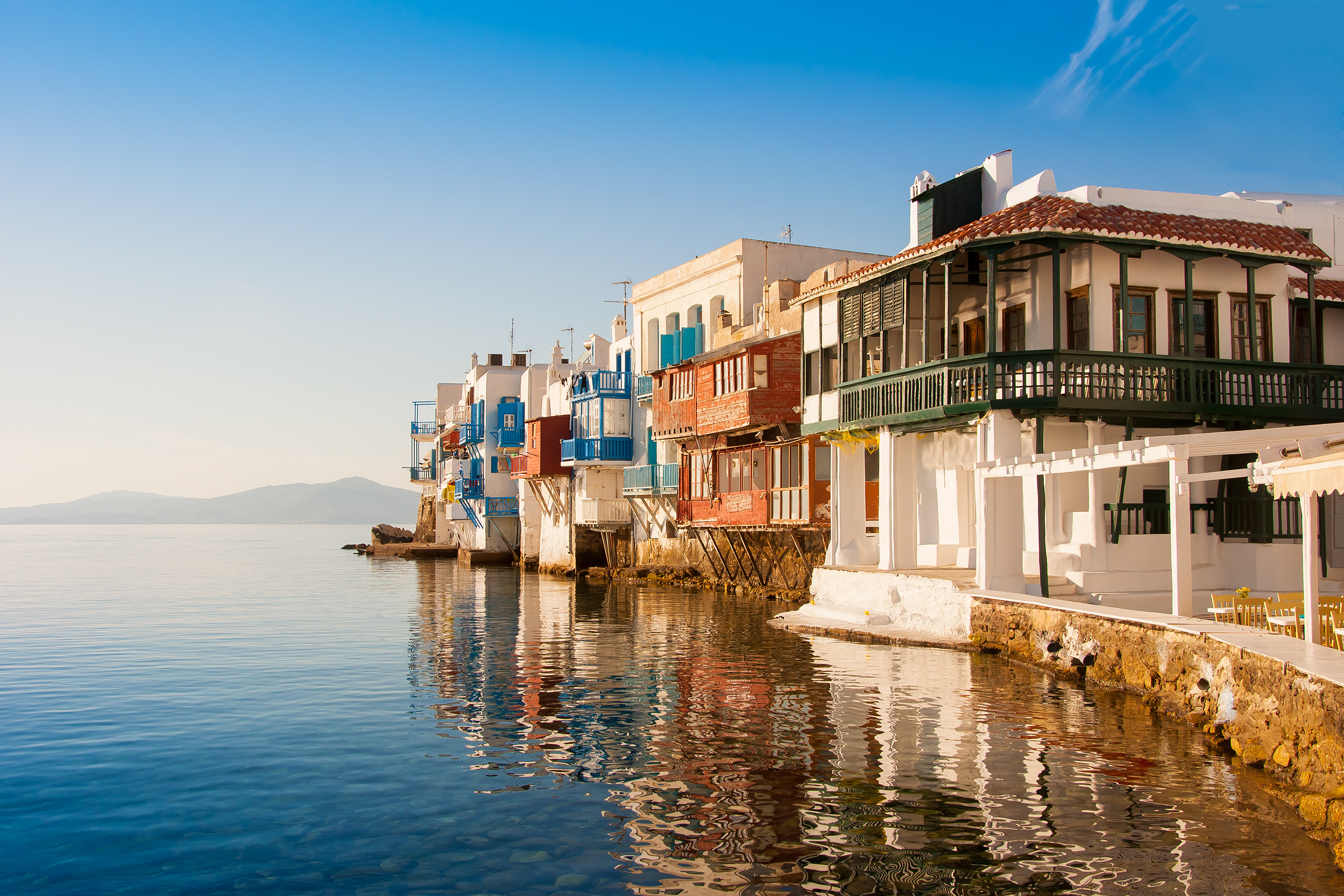 Seaside view of Little Venice in Mykonos, Greece, with colorful balconies over the Aegean waters at sunset.