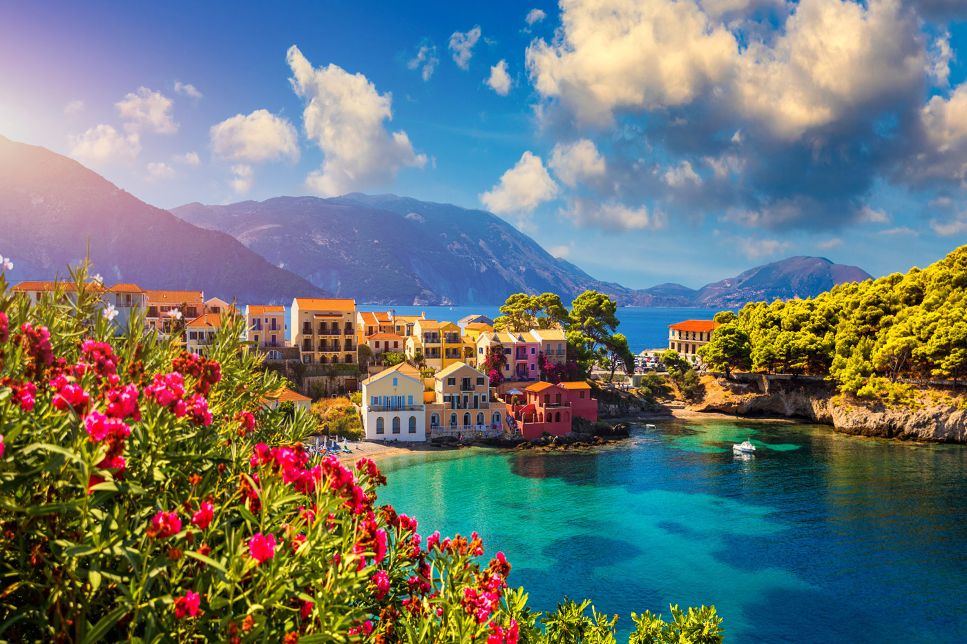 Colorful coastal village in Kefalonia, Ionian Islands, Greece, with turquoise waters, flowers, and mountain backdrop.