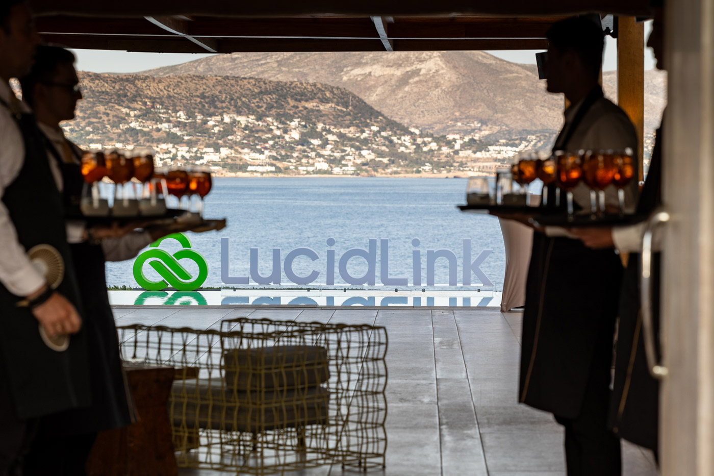 Luxury corporate event in Greece — seaside cocktail reception with waiters serving drinks and branded LucidLink logo by the pool, organized by a DMC agency.