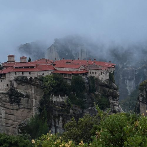 Meteora monastery perched on dramatic rock cliffs, surrounded by mist and clouds, symbolizing reflection, legacy, and timeless leadership.