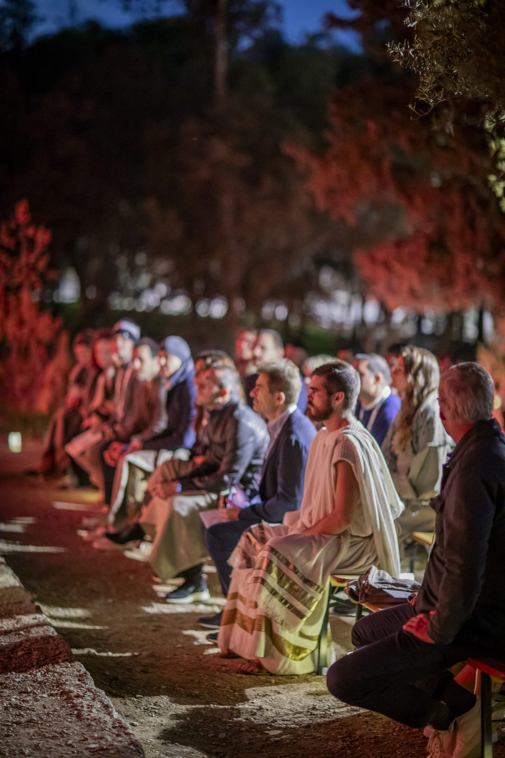 Audience watching an immersive night performance set in ancient Athens, with actors in traditional Greek attire at a historic outdoor venue.