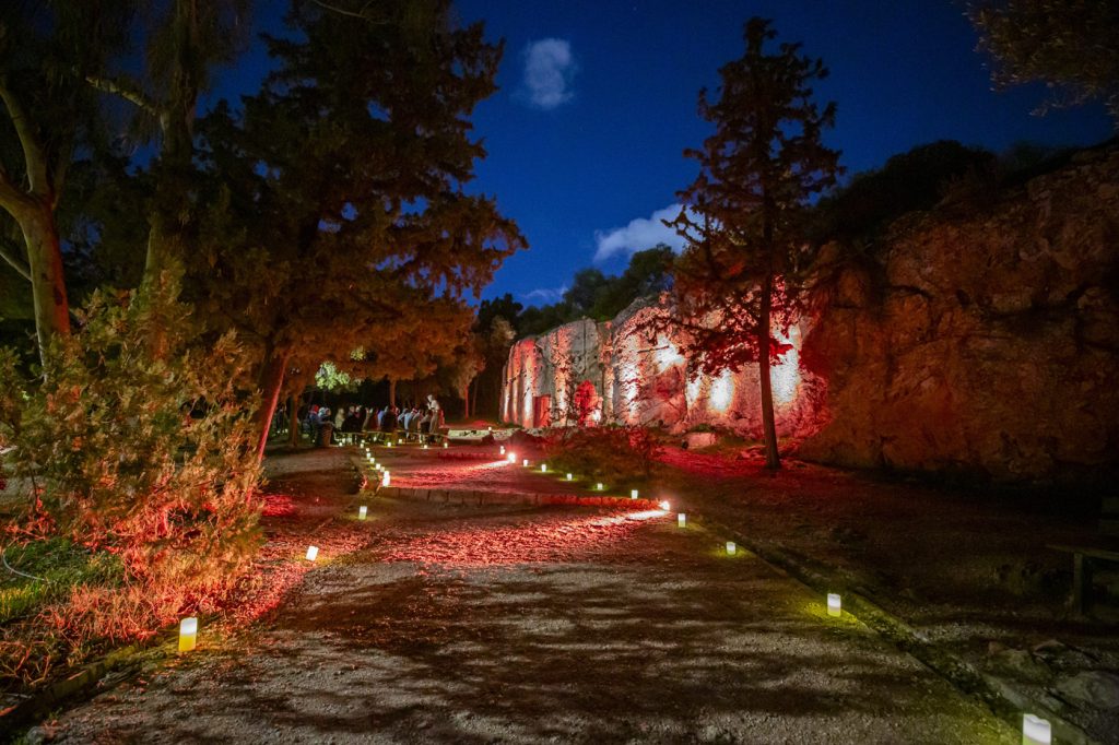 Candle-lit pathway leading to the illuminated Prison of Socrates in Athens during an immersive nighttime experience.